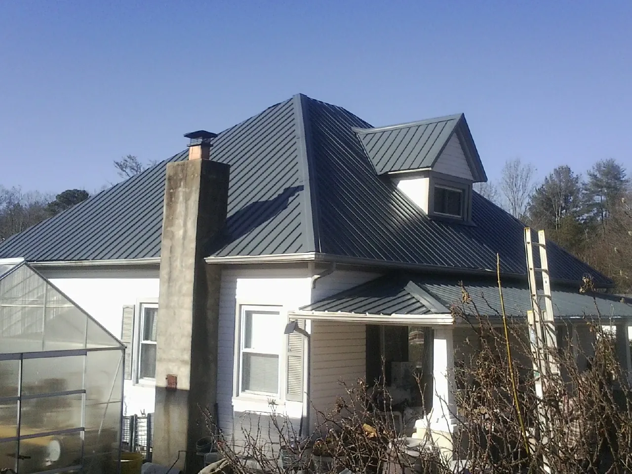 Dark blue standing seam metal roof on a white farmhouse with dormer — Slate & Tile Roof Repair by Roofing Brothers in Sims
