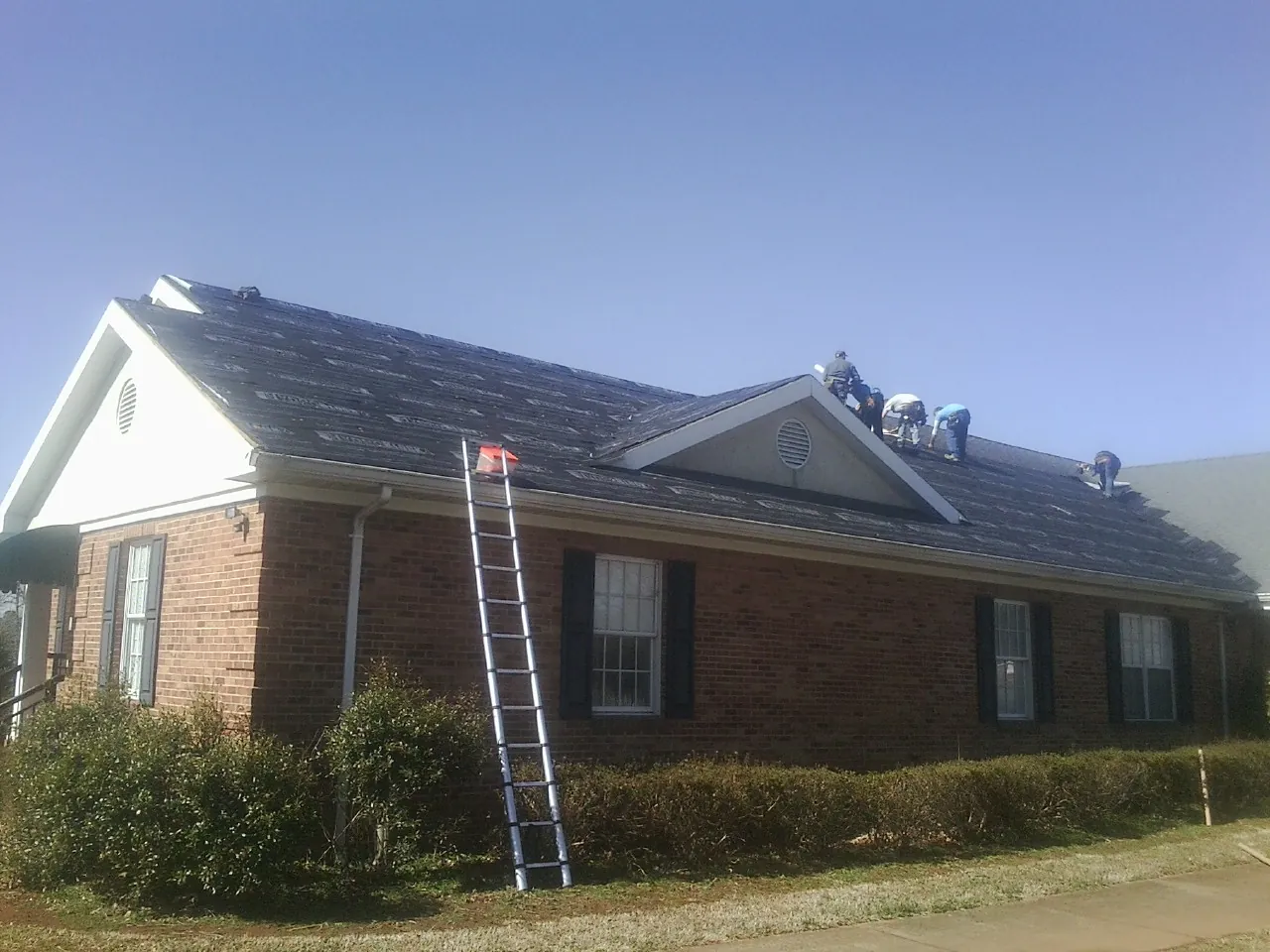 Crew tearing shingles off a brick ranch roof with a ladder set — Metal Roof Repair work by our crew in Sims