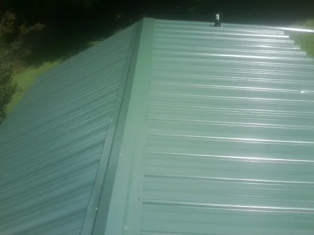 New green metal panels meeting at the ridge of a roof — Flat Roof Repair work by our crew in Sims
