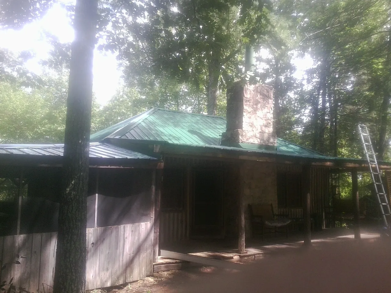 Green metal roof and stone chimney above a log cabin porch in Sims