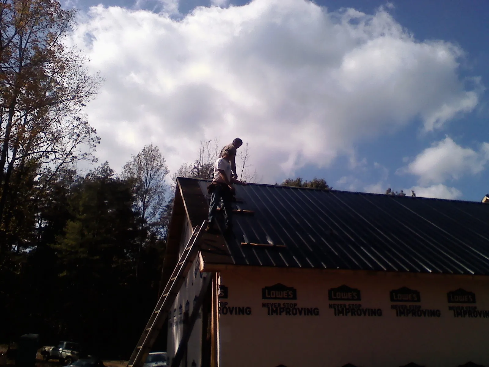 Roofer fastening dark metal panels high against a cloudy sky, from a Roof Inspection job in Sims